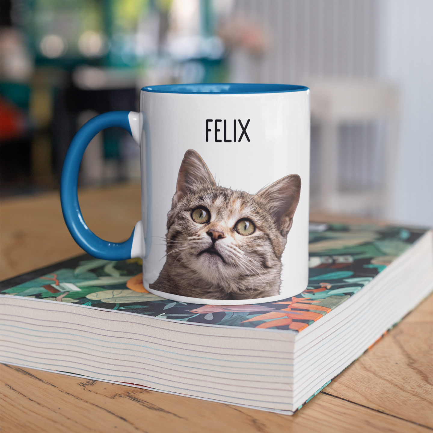 Personalized mug featuring a tabby cat with the name 'Felix' above. The mug has a blue handle and interior, displayed on a stack of books, perfect for custom cat photo and name gifts.