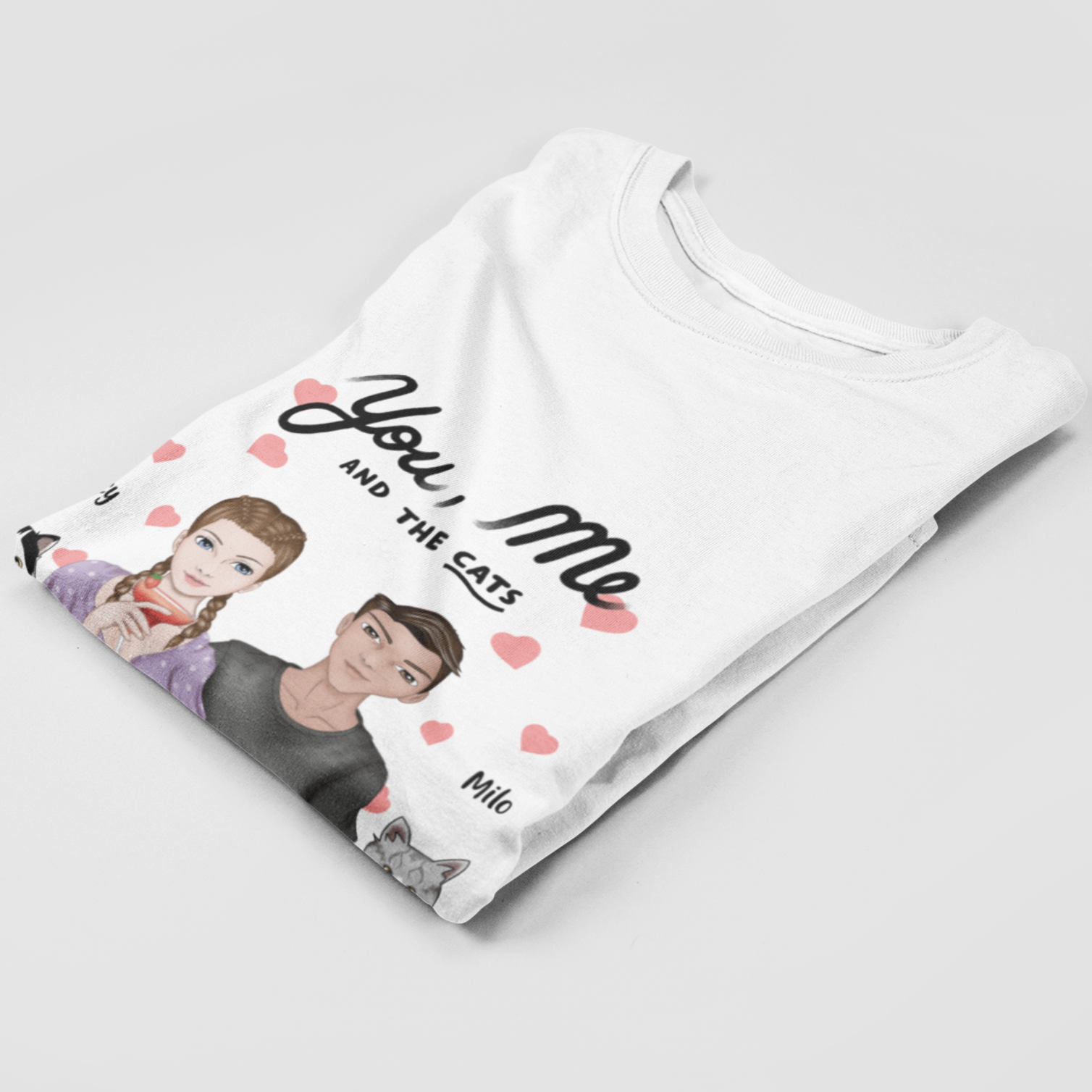 Folded t-shirt displaying the 'You, Me AND THE CATS' design with personalized woman and man characters and two custom cat images, each with their chosen name above.